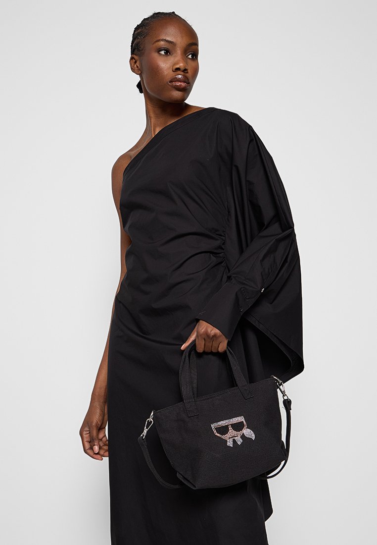 Sac à main en tissu noir avec une forme structurée, orné d'un design de lunettes de soleil en strass. Dispose de poignées doubles et d'une bandoulière amovible.