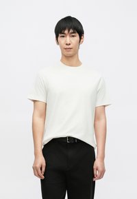 Bílé bavlněné tričko s kulatým výstřihem, krátkými rukávy a volným střihem, doplněné černými kalhotami a černým páskem.