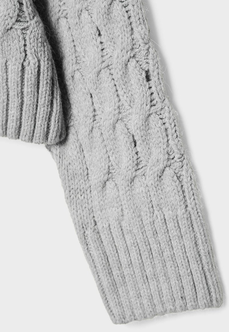 Manica di un maglione grigio lavorato a maglia con un motivo a treccia e polsini a costine, che mette in risalto la texture morbida e una vestibilità aderente.