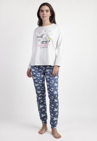 Camisa de pijama blanca de manga larga con un gráfico de Snoopy y Woodstock, combinada con pantalones de pijama azules con patrones de muñecos de nieve y puntos.