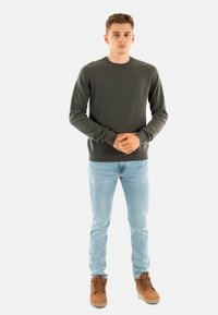 Maglione grigio a maglia con scollatura a girocollo, polsini e orlo a coste. Abbinato a jeans azzurri e stivali marroni stringati.