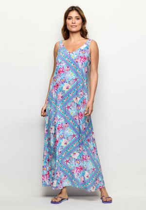 Maxime dress in light blue fabric featuring floral and seashell patterns, with a V-neck and wide straps, paired with purple sandals.