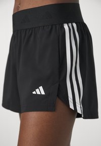 Svarta sportshorts med en bred svart midja. Har tre vita vertikala ränder på ena sidan och en liten vit logotyp nära fållen.