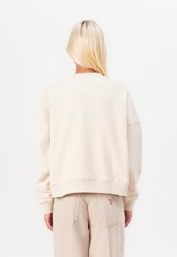Felpa beige chiaro con vestibilità comoda, polsini e orlo a costine, e una texture morbida. Il retro presenta dettagli di design minimalisti.