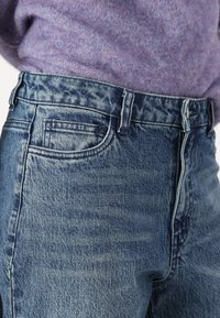 Jean en denim de couleur bleu délavé avec un design classique à cinq poches, présentant une coupe droite et des détails de couture visibles.