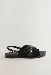 Črna sandal z mešanico semiša in teksturiranega sintetičnega materiala. Oblikovanje poudarjajo križno prepleteni trakovi in nastavljiv zaponka.