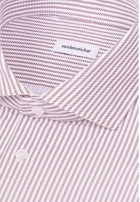 Gros plan d'une chemise blanche à fines rayures diagonales marron, montrant le col, les boutons et une étiquette portant la mention seidensticker.