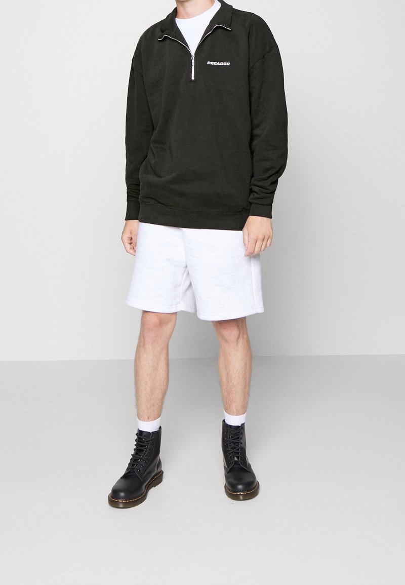 Černá mikina na zip s logem "PEGALDOR", kombinovaná se světle šedými šortkami. Černé šněrovací boty, bílé ponožky, stojící na neutrálním pozadí.