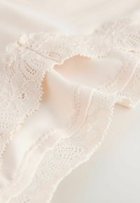 Tissu beige doux avec bordure en dentelle complexe et couture délicate, montrant une texture et un motif détaillés en vue rapprochée.