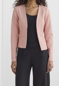 Ljust rosa, figursydd blazer med en slät textur och öppen design framtill, ihopparad med en svart topp och svarta vida byxor.