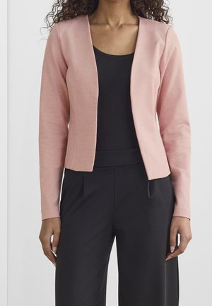 Světlý růžový, přiléhavý blazer s hladkou texturou a otevřeným předním designem, spojený s černým topem a volnými černými kalhotami.