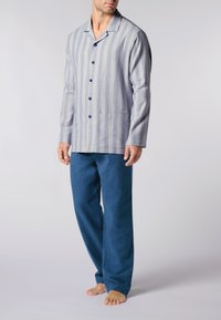 Camicia a righe blu e bianca a maniche lunghe con bottoni e tasche a toppa, abbinata a pantaloni blu scuro. Tessuto morbido, vestibilità rilassata.