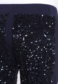 Marina byxor med en sidopanel dekorerad med paljetter, med en slät textur och en glittrande finish på paljetterna.