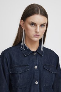 Σκούρο τζιν μπουφάν με δύο τσέπες στο στήθος, κουμπιά μπροστά και γιακά. Διαθέτει μακριά, ασημένια σκουλαρίκια με περίπλοκο σχέδιο.