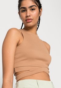 Top cropped canelado em tom cáqui com gola alta e design sem mangas, apresentando um detalhe torcido na bainha.
