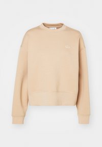 Sudadera corta beige hecha de un material suave, con un escote redondo y puños acanalados. Pequeño detalle del logo en el pecho.