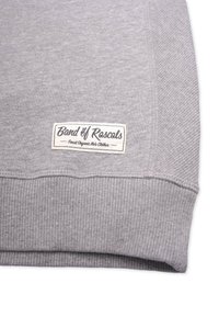 Grå sweatshirt med ribbad nederkant och ärmslut. Har en rektangulär vit etikett med "Band of Rascals"-logotyp och text, som indikerar ekologiska barnkläder.