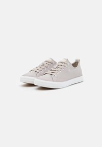 Ljust grå canvas sneakers med rund tå, vit gummisula, snörningsfront och en liten logodetalj på sidan. Plant, texturerat tyg.