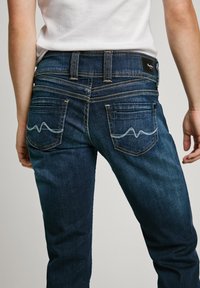 Mørkeblå denim jeans med slim fit, med subtile bølgestikking på baklommene og kontraststing langs sømmene.