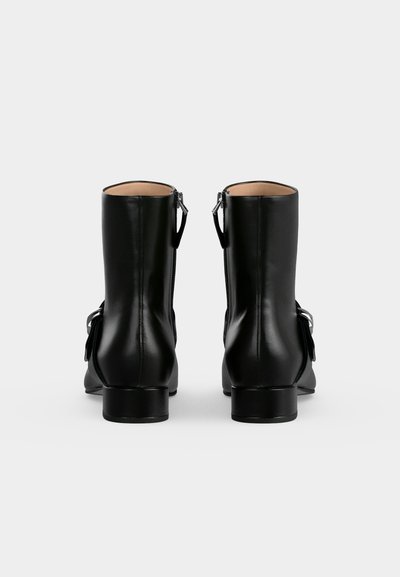 Paire de bottines en cuir noir avec fermetures éclair au dos et bas talons carrés, vues de dos sur un fond clair uni.