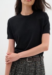Maglione a maniche corte nero in maglia con scollo rotondo, abbinato a una gonna a spina di pesce testurizzata e una cintura in pelle marrone.