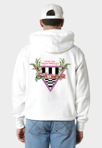 Biała bluza z kapturem z kolorową grafiką na plecach, przedstawiającą kratkowany wzór, tropikalne liście oraz czerwoną wyścigówkę w trójkącie.