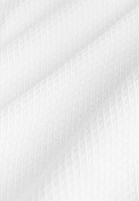 Hvid tekstureret stof med et geometrisk mønster, der har hævede diamantformer og en glat overflade, draperet i bløde folder.