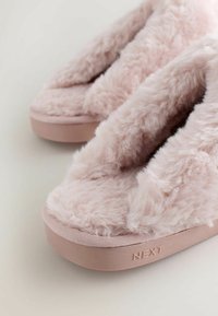 Roze pluizige pantoffels met een zacht, donzig oppervlak en een vlakke rubberen zool, met de merknaam "NEXT" in reliëf aan de zijkant.