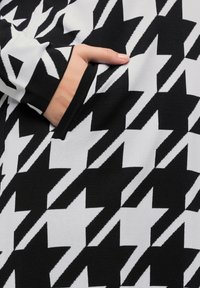 Zwart-wit houndstooth-patroon stof met een zachte textuur, met een zijzak laag aan het kledingstuk.