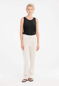 Top nero a coste senza maniche abbinato a pantaloni beige con coulisse. I pantaloni presentano una vestibilità comoda e gambe dritte, indossati con ciabatte nere.
