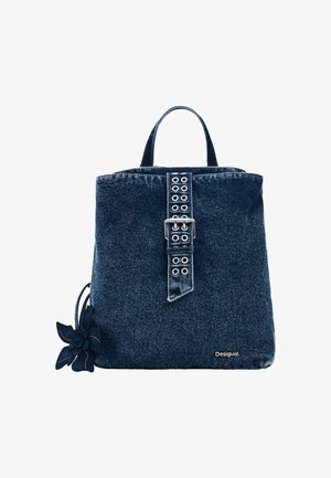 Mochila de mezclilla en azul oscuro con una correa de hebilla y ojales metálicos. Acentuada con un detalle de flor de tela en el lateral.