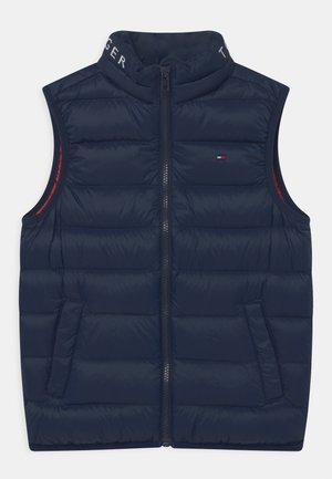 Chaleco sin mangas acolchado de color azul marino con un alto cuello, cremallera frontal y bolsillos laterales. El interior presenta un forro rojo en contraste.
