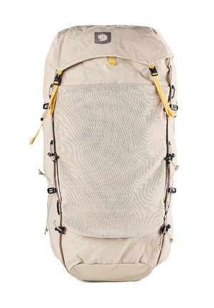 Sac à dos de randonnée beige avec grande poche avant en filet, bretelles jaunes réglables, boucles latérales et rabat supérieur avec écusson logo.