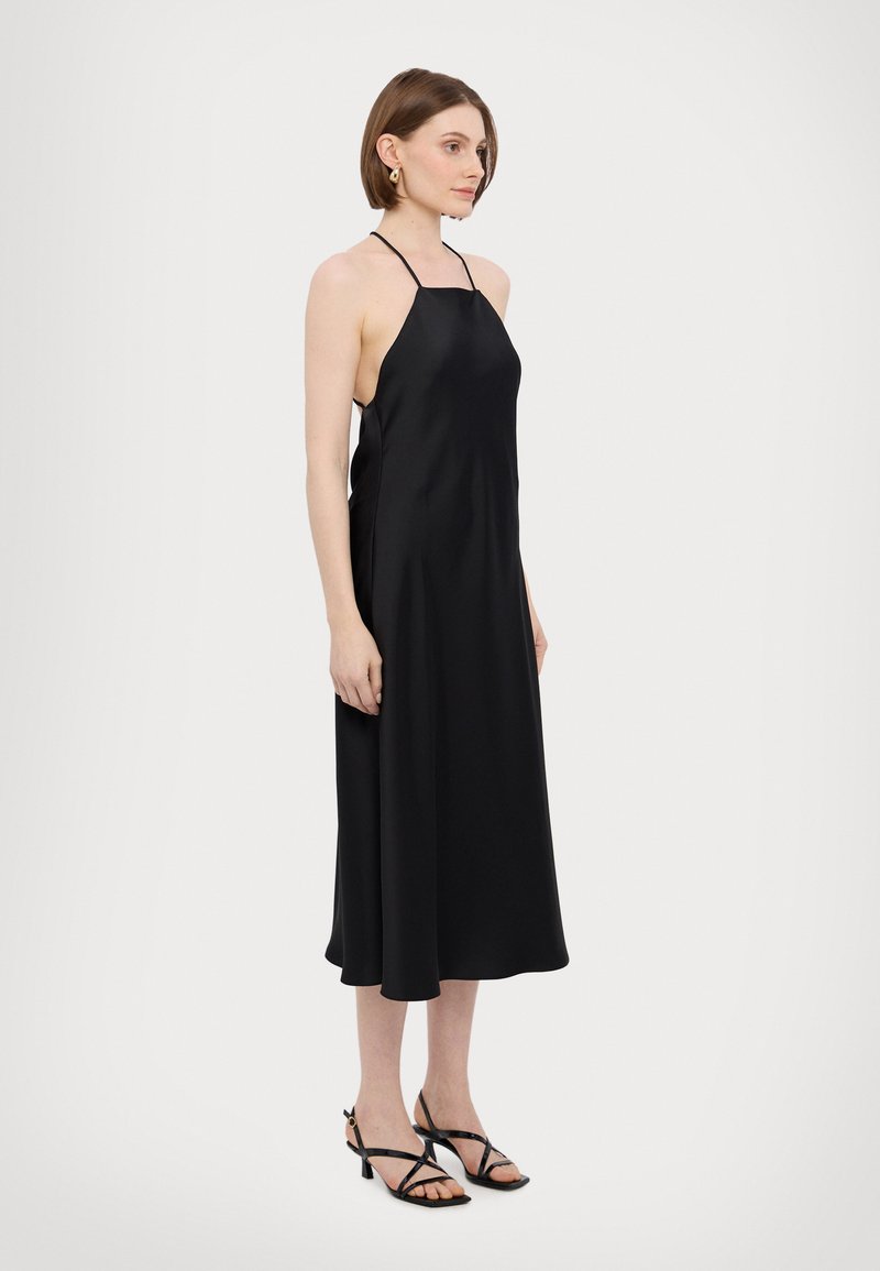Black satin halter dress with a flowing A-line silhouette. Features thin straps and a smooth texture, paired with strappy black heels.