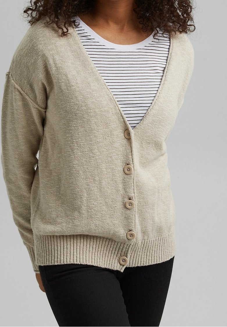 Cardigan beige a maglia con scollo a V, cinque bottoni e orlo a costine; indossato sopra una maglietta a righe, con maniche leggermente oversize.