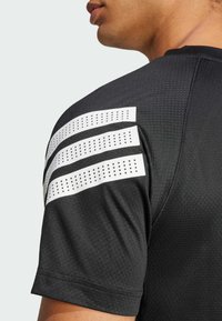 Camiseta deportiva negra con tejido texturizado, mangas cortas y tres acentos de rayas blancas con perforaciones en el hombro.
