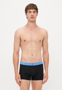 Schwarze Boxershorts mit einem hellblauen Bund, auf dem das Logo "TOMMY HILFIGER" zu sehen ist. Glattes, dehnbares Material. Niedrig sitzendes Design.