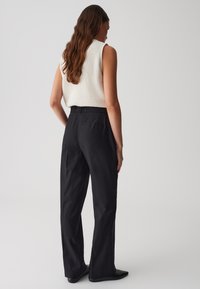 Pantalons larges noirs à taille haute, dotés de poches latérales et d'une texture lisse. Le modèle porte un débardeur en tricot léger.