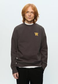 Brown sweatshirt with a crew neckline, featuring a yellow logo on the chest. Long sleeves, ribbed cuffs, and medium weight fabric.