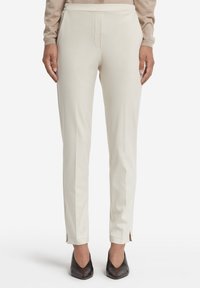 Pantaloni slim-fit color crema con fessure laterali all'orlo, caratterizzati da una superficie liscia e un design minimalista.