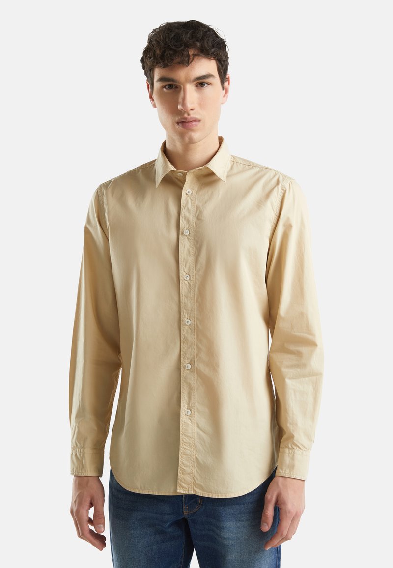 Lange mouwen, knoopshirt in lichtbeige katoen. Beschikt over een klassieke kraag, knopen aan de voorkant en een rechte zoom. Draagt met blauwe jeans.
