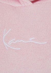 Roze, textiel met een reliëf witte cursieve logo. Het materiaal lijkt zacht en plush, geschikt voor casual draag.