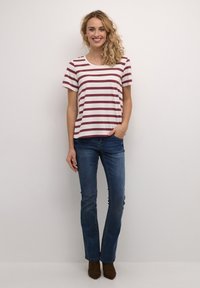 Gestreepte t-shirt met korte mouwen in crème en kastanjebruin, met een ronde halslijn, gecombineerd met donkerblauwe jeans en bruine enkellaarsjes.