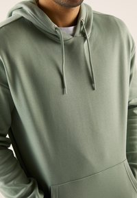 Felpa verde chiaro realizzata in materiale morbido, con cappuccio regolabile, tasca a marsupio e polsini a coste, senza alcun motivo o etichetta visibile.