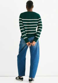 Green striped sweater with white stripes, ribbed cuffs, paired with loose-fitting blue denim jeans and black sneakers. Textured knit design.