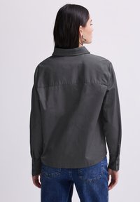 Grijze katoenen shirt met een kraag, rugpand en decoratieve stippen. Voorzien van knoopmanchetten en een ontspannen pasvorm. Gecombineerd met blauwe spijkerbroeken.