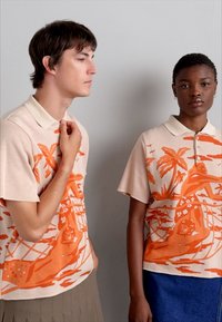 Korte mouwen polo-shirts in lichtbeige met een oranje tropisch patroon; zachte textuur, contrasterende kraag en een relaxte pasvorm.