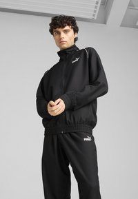 Black athletic tracksuit made of smooth fabric, featuring zippered jacket with high collar, elastic cuffs, and waistband, adorned with white logo.
