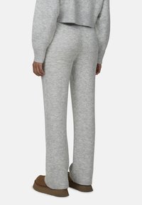 Jasnoszare, dzianinowe spodnie loungewear o luźnym kroju, z prążkowanym pasem i miękką teksturą. Połączone z brązowym obuwiem.