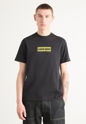 Zwarte katoenen t-shirt met een rechthoekig geel logo met de tekst "calvin klein new york city" op de voorkant. Korte mouwen, ronde halslijn.